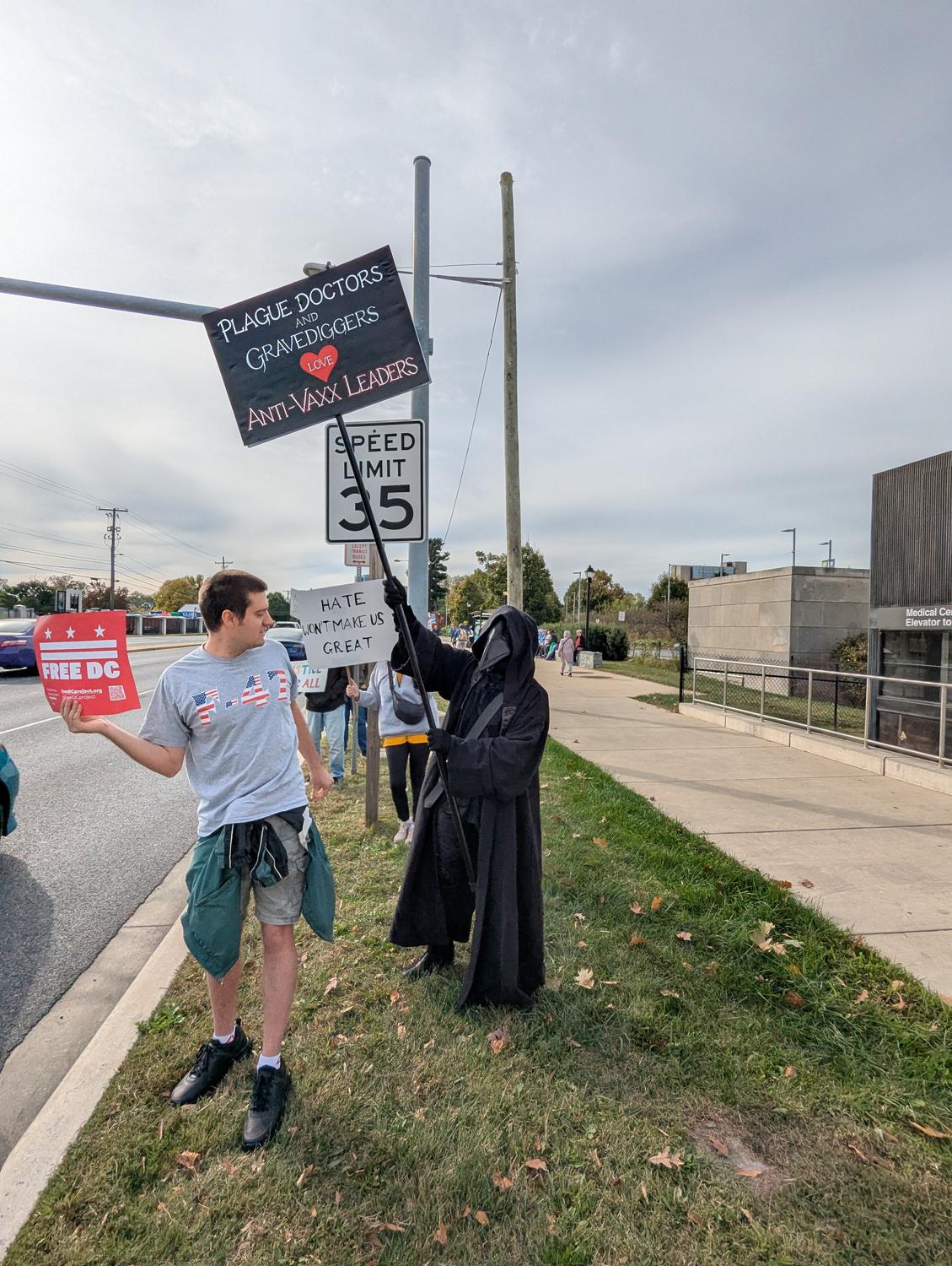 Person in Plague Doctor Costume 
Sign says Plague Doctors and Gravediggers lover Anti-VAXX Leaders